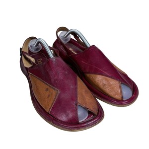 May include: A pair of two-tone leather sandals featuring a deep burgundy and tan color-blocked design. These open-toe sandals include a slingback strap with a buckle closure and a metallic shoe tree insert inside each shoe to maintain their shape.