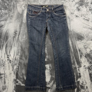 May include: Dark blue denim jeans featuring a low-rise waist, a button and zipper fly closure, and a slight flare at the leg openings. The jeans include front pockets with decorative stitching and a small branded label on the inner waistband.