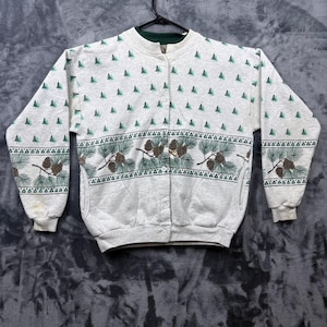 May include: A light gray long-sleeve button-up sweatshirt featuring a repeating pattern of small green pine trees on the upper section and a horizontal band across the chest and sleeves displaying detailed illustrations of pine cones and needles.