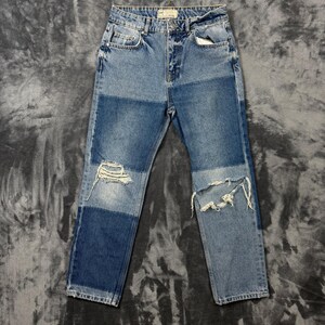May include: High-waisted blue denim jeans featuring a colour-blocked design with alternating light and medium wash panels. The jeans include a classic five-pocket construction, a button and zip fly closure, and distressed detailing at both knees.