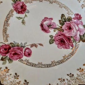 May include: A white porcelain serving platter with a scalloped edge and two handles. The platter is decorated with pink roses and gold accents. The roses are clustered in the center and along the edge of the platter.