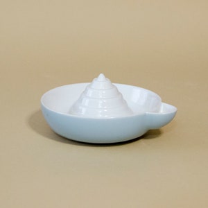 May include: A white ceramic citrus juicer with a light blue base. The juicer has a cone-shaped reamer with ridges for squeezing lemons and limes.