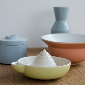 May include: A set of four ceramic kitchenware items in blue, white, and yellow. The set includes a small covered jar, a large bowl, a small bowl, and a citrus juicer.
