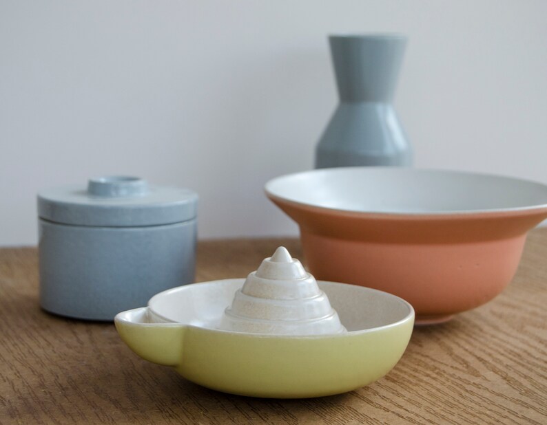 May include: A set of four ceramic kitchenware items in blue, white, and yellow. The set includes a small covered jar, a large bowl, a small bowl, and a citrus juicer.