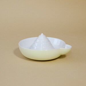 May include: A white ceramic citrus juicer with a cone-shaped reamer and a yellow base.