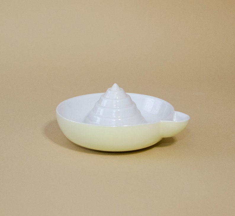 May include: A white ceramic citrus juicer with a cone-shaped reamer and a yellow base.