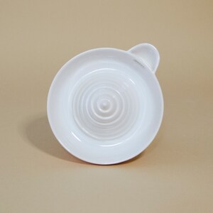 May include: White ceramic citrus juicer with a ridged surface and a small handle. The juicer is designed to extract juice from lemons, limes, and oranges.