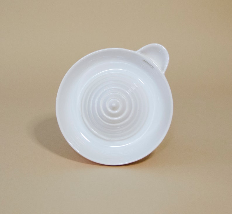 May include: White ceramic citrus juicer with a ridged surface and a small handle. The juicer is designed to extract juice from lemons, limes, and oranges.