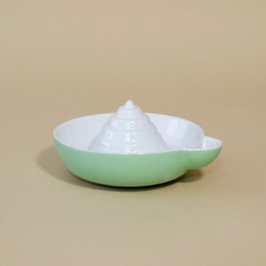 May include: A green ceramic citrus juicer with a white cone-shaped reamer in the center.
