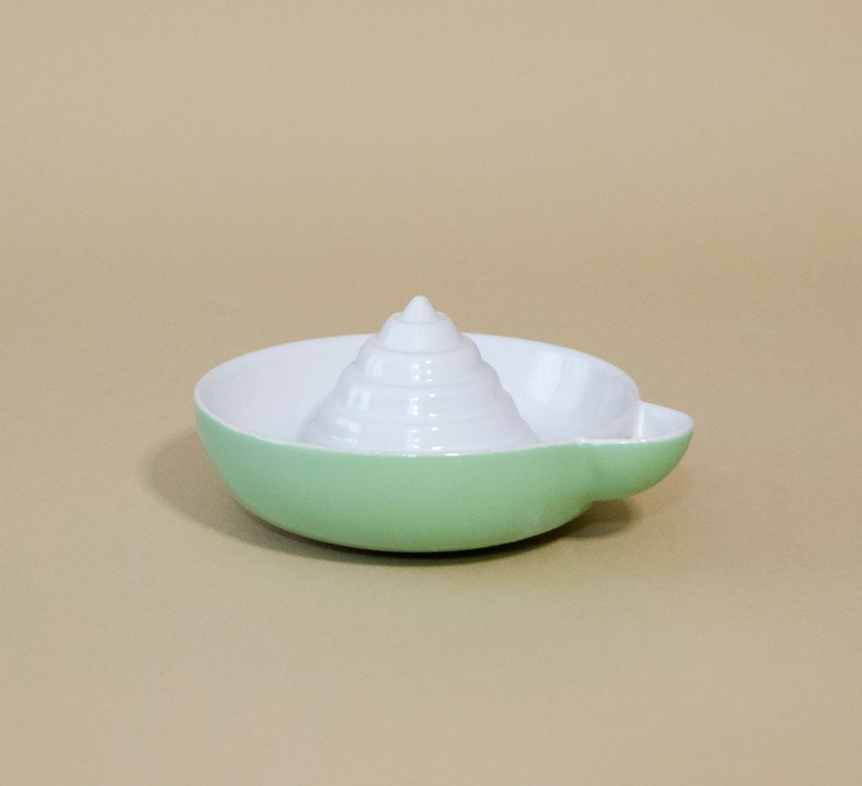 May include: A green ceramic citrus juicer with a white cone-shaped reamer in the center.