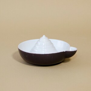 May include: A white and dark gray ceramic citrus juicer with a cone-shaped reamer in the center.