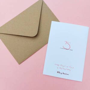 May include: A white card with a pink illustration of a cat with a speech bubble that says "I'm not a morning person". The card is on a pink background. The back of the card has the text "Lovingly Designed and Printed by Ally-Dery Hubbert @Burg_Illustrations".