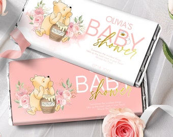 May include: Pink and white baby shower chocolate bar wrappers featuring Winnie the Pooh with a honey pot and floral designs. The text on the wrapper reads "Olivia's Baby Shower".