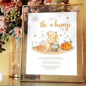 May include: A printable sign with a cartoon Winnie the Pooh bear holding a jar of honey. The sign says "A message from the heart bump" and includes a poem about the baby's arrival. The background is a fall theme with pumpkins and leaves.