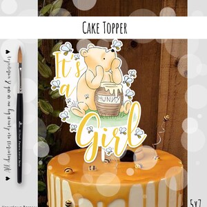 Könnte beinhalten: Ein Tortenaufsatz mit Winnie-the-Pooh-Motiv und dem Text "It's a Girl". Das Design umfasst einen Cartoon-Bären, einen Honigtopf und Bienen. Der Kuchen ist mit Honig und bienenförmigen Dekorationen verziert.
