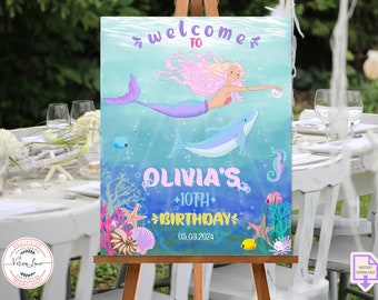 May include: A welcome sign for a 10th birthday party with a mermaid and dolphin illustration. The sign is blue and green with a pink and purple mermaid. The text on the sign reads "Welcome to Olivia's 10th Birthday 05.03.2024".