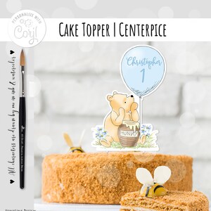 May include: A Winnie the Pooh themed cake topper featuring a cartoon Winnie the Pooh holding a jar of honey. A blue balloon with the text "Christopher 1" is attached to the balloon. The topper is on a cake with a bee decoration.