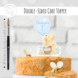 May include: Double-sided cake topper featuring a Winnie the Pooh character holding a honey pot with a blue balloon that says "Christopher 1".