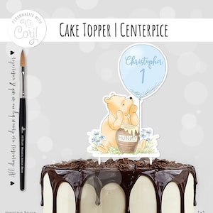 May include: A Winnie the Pooh cake topper with a blue balloon that says "Christopher 1" and a honey pot. The topper is on a chocolate cake with white frosting.