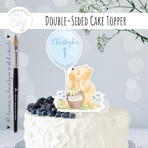 May include: Double-sided cake topper featuring a Winnie the Pooh character holding a honey pot. The balloon is blue and says "Christopher 1".