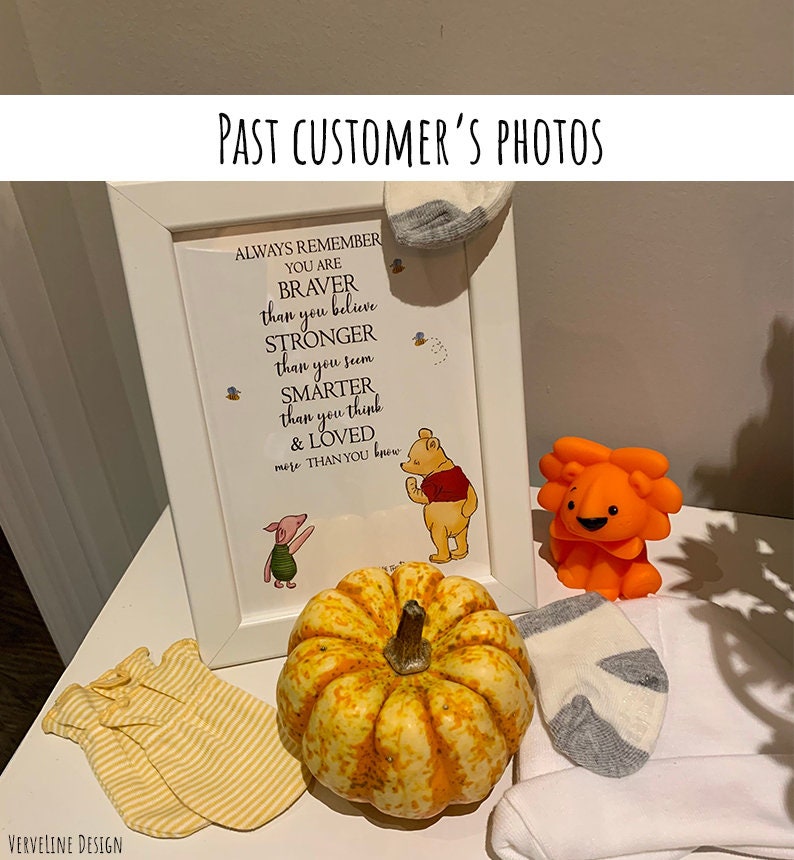 May include: A framed Winnie the Pooh quote that reads "Always remember you are braver than you believe, stronger than you seem, smarter than you think & loved more than you know."  The frame is on a white table with a small pumpkin, a stuffed lion, and two pairs of baby socks.