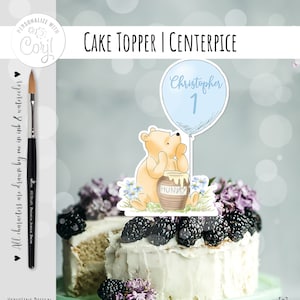 May include: Winnie the Pooh cake topper with a blue balloon that says "Christopher 1" and a honey pot. The topper is on a white cake with blackberries and purple flowers.