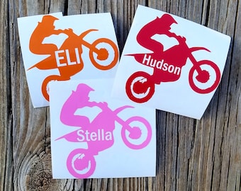 May include: Three motocross rider decals with personalized names. The decals are orange, red, and pink. The decals feature a silhouette of a rider on a dirt bike.