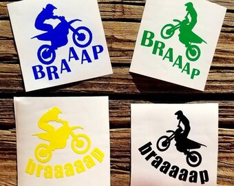 May include: Four motocross decals with different colored silhouettes of a rider on a dirt bike. The decals have the word "BRAAAP" written underneath the bike in different styles.