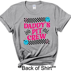Puede incluir: Camiseta gris con un patr&oacute;n de cuadros blanco y negro, texto rosa que dice "Daddy's Pit Crew" y caras sonrientes azules.