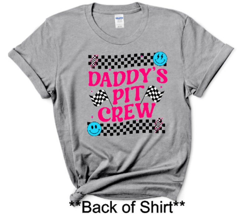 Puede incluir: Camiseta gris con un patr&oacute;n de cuadros blanco y negro, texto rosa que dice "Daddy's Pit Crew" y caras sonrientes azules.