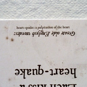 May include: A close-up of a vintage-style paper with the words "heart-quake" and "Greate oide Englysh wordes" printed in dark brown. The text "heart-quake: a palpitation of the heart" is also visible. The paper has a distressed, aged appearance.