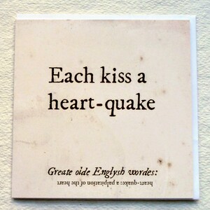 May include: Square card with the text "Each kiss a heart-quake" in black font. The card has a vintage, aged paper appearance with the words "Greate oide Englysh wordes: heart-quake: a palpitation of the heart" at the bottom.