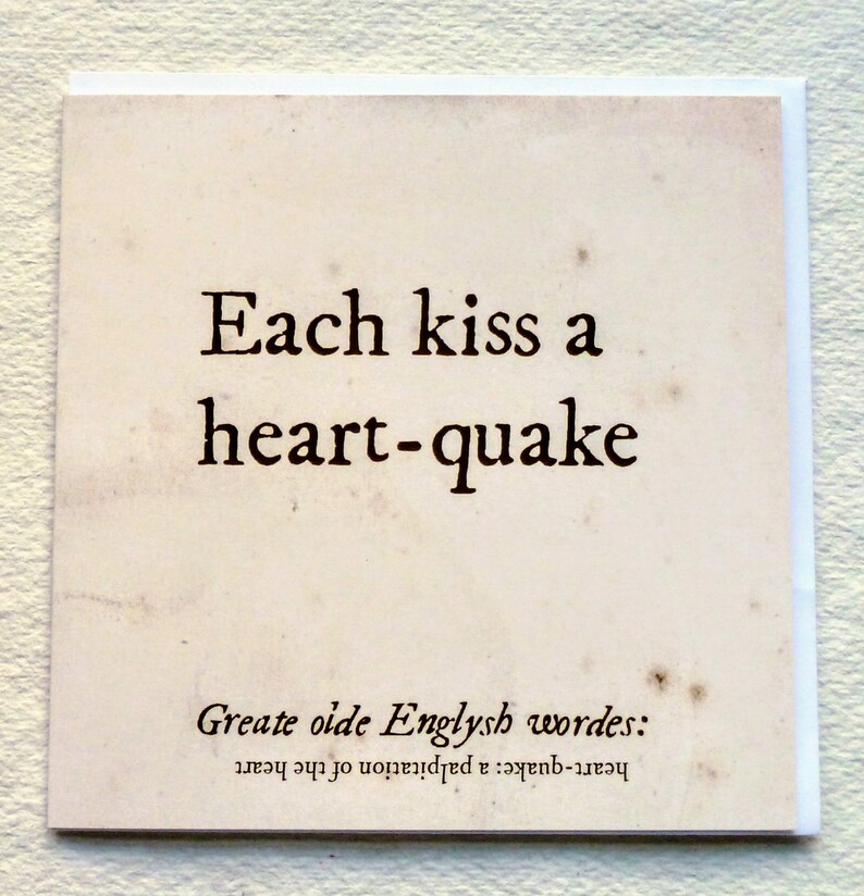 May include: Square card with the text "Each kiss a heart-quake" in black font. The card has a vintage, aged paper appearance with the words "Greate oide Englysh wordes: heart-quake: a palpitation of the heart" at the bottom.