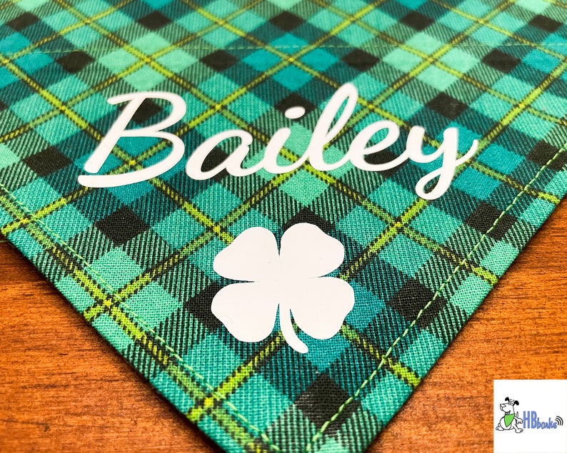 May include: Green and black plaid fabric dog bandana with the name "Bailey" and a white four-leaf clover.
