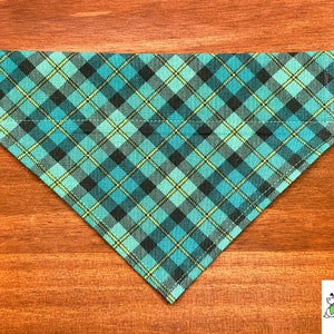 May include: A turquoise, black, and yellow plaid dog bandana. The bandana is triangular in shape and has a stitched edge.