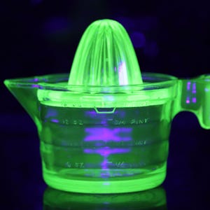 May include: A vintage, neon green glass juicer with a conical reamer and a measuring cup base. The juicer has a handle and spout for easy pouring. The measurements are in ounces and pints. The background is dark.