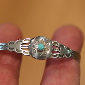 May include: A silver-toned bracelet with a central floral design and a small turquoise stone. The bracelet has a delicate, openwork design with scalloped edges and measures approximately 6 inches in circumference.