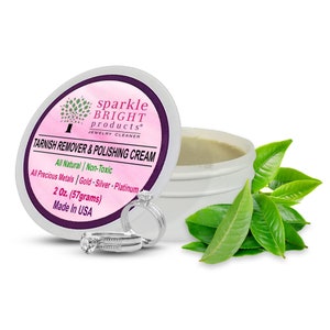 May include: A white jar of Sparkle Bright Products tarnish remover and polishing cream with a pink label. The label reads Tarnish Remover & Polishing Cream, 2 Oz. (57grams), Made In USA. Two silver-toned rings and green tea leaves are visible.