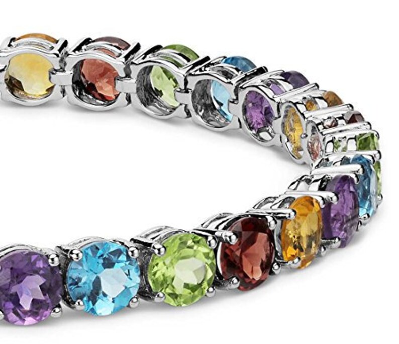 Puede incluir: Una pulsera de plata con una fila de piedras preciosas de colores. Las piedras est&aacute;n engastadas en una banda de plata y est&aacute;n dispuestas en un patr&oacute;n de arco&iacute;ris. La pulsera es una pieza de joyer&iacute;a hermosa y &uacute;nica.
