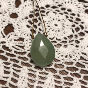 May include: A green gemstone pendant on a brown cord necklace. The pendant is faceted and has a teardrop shape.