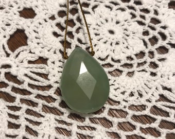 May include: A green gemstone pendant on a brown cord necklace. The pendant is faceted and has a teardrop shape.