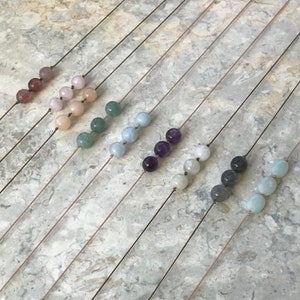 May include: A set of ten necklaces featuring various coloured gemstone beads. Each necklace has a single strand of beads and a simple, minimalist design.