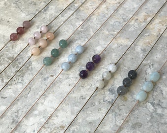 May include: A set of ten necklaces with different colored gemstone beads. Each necklace has a single strand of beads and a simple, minimalist design.