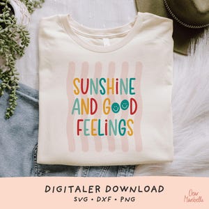 Può includere: Una t-shirt color crema con un design grafico a righe verticali ondulate rosa chiaro. Il testo SUNSHINE AND GOOD FEELINGS è scritto con un carattere multicolore, con due piccole faccine sorridenti che sostituiscono la lettera O.