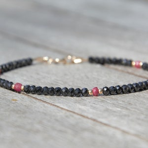 Könnte beinhalten: Ein zartes Armband aus schwarzen Edelsteinperlen und zwei kleinen rosa Perlen.