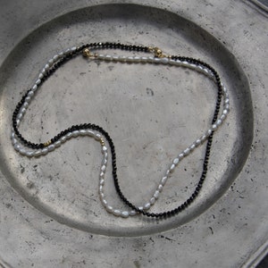 Op de afbeelding: Een witte parelketting en een zwarte edelsteenketting gelegd op een zilveren bord.