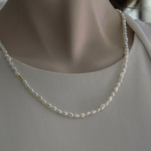 Op de afbeelding: Een eenvoudige witte parelketting met een gouden accent. De ketting ligt op een witte achtergrond.