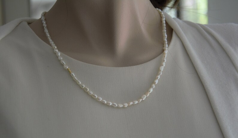 Op de afbeelding: Een eenvoudige witte parelketting met een gouden accent. De ketting ligt op een witte achtergrond.