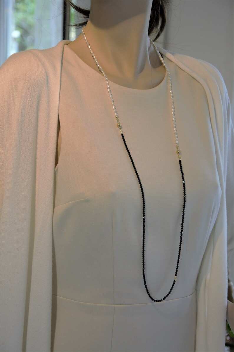 Op de afbeelding: Een lange ketting met zwarte en witte kralen. De ketting is gemaakt van kleine, ronde kralen en heeft een gouden sluiting.