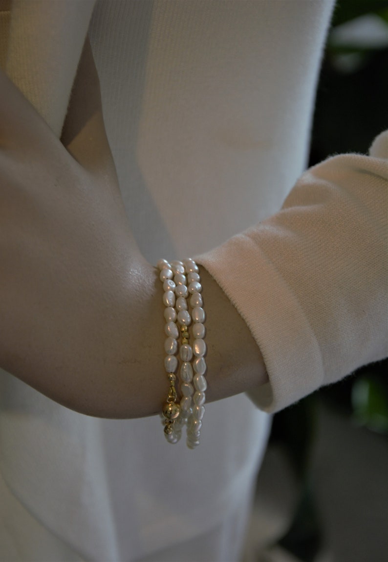 Op de afbeelding: Een set van drie parel armbanden met gouden accenten. De armbanden zijn op elkaar gelegd op iemands pols.